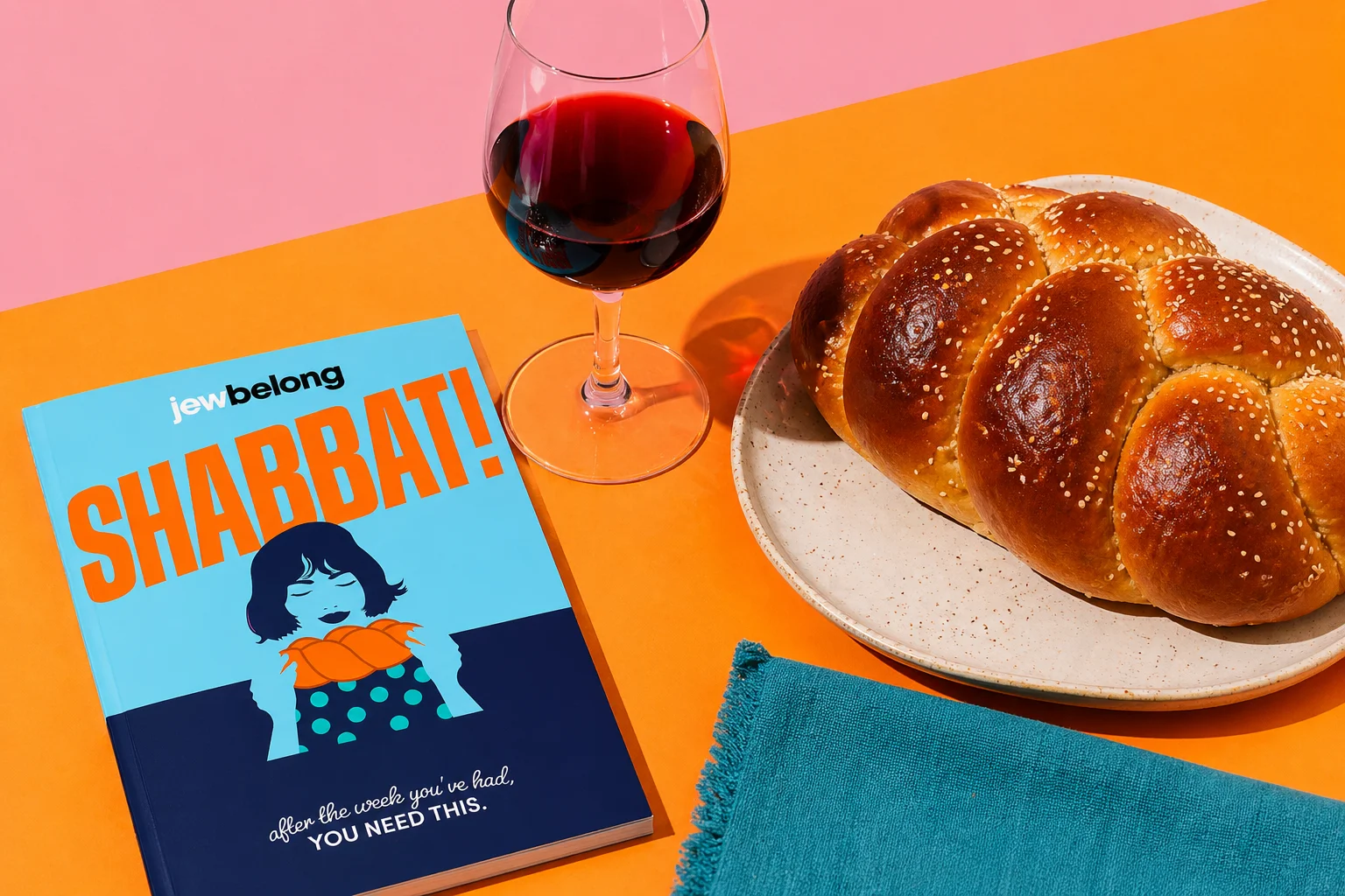 Bright, modern Shabbat table scene with braided challah, a glass of red wine, and the JewBelong Shabbat booklet on a colorful background with bold lighting and shadows.